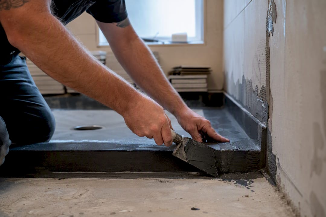 Hands applying waterproof membrane in ensuite bathroom